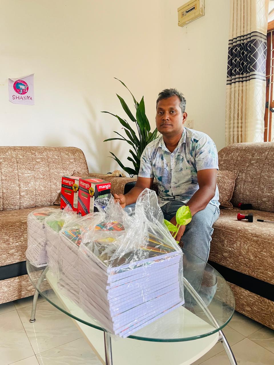 NMF representative with stacks of school notebooks prepared for educational support in Pottuvil.